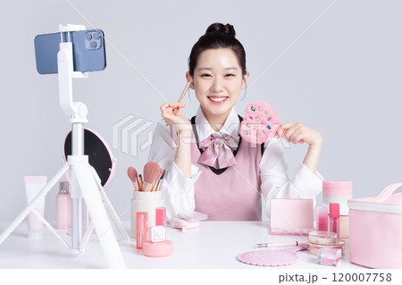 A teenage woman in school uniform laying out various cosmetics and filming a video with her smartphone A teenage woman in school uniform laying out various cosmetics and filming a video with her smartphone 120007758