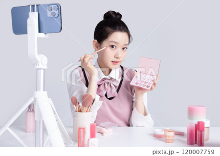 A teenage woman in school uniform laying out various cosmetics and filming a video with her smartphone A teenage woman in school uniform laying out various cosmetics and filming a video with her smartphone 120007759