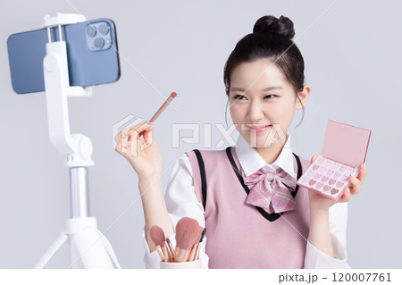 A teenage woman in school uniform laying out various cosmetics and filming a video with her smartphone A teenage woman in school uniform laying out various cosmetics and filming a video with her smartphone 120007761