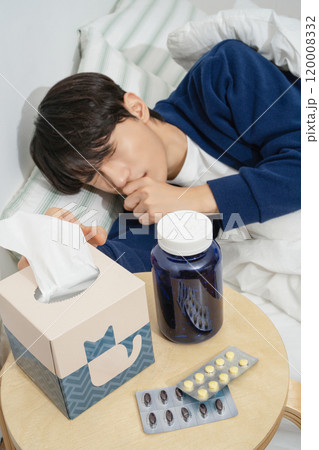 A man in his 20s coughing while lying in bed because he is sick A man in his 20s coughing while lying in bed because he is sick 120008332