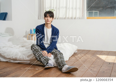 A man in his 20s sitting on a bed in comfortable clothes A man in his 20s sitting on a bed in comfortable clothes 120008354