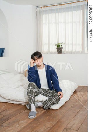 A man in his 20s sitting on a bed in comfortable clothes 120008364