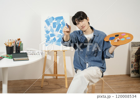 A man in his 20s painting on canvas with paints 120008534