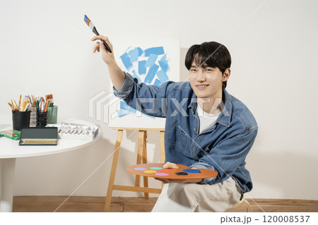 A man in his 20s painting on canvas with paints 120008537