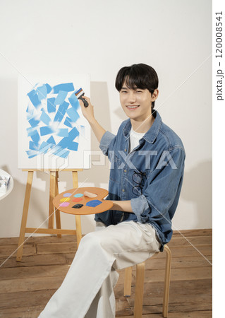 A man in his 20s painting on canvas with paints 120008541