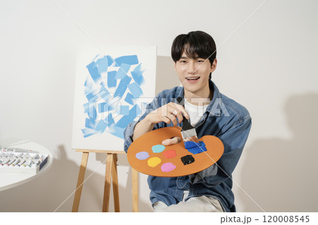 A man in his 20s painting on canvas with paints 120008545