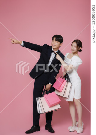 A couple wearing dresses and suits and holding shopping bags 120009953