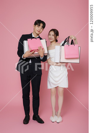 A couple wearing dresses and suits and holding shopping bags A couple wearing dresses and suits and holding shopping bags 120009955