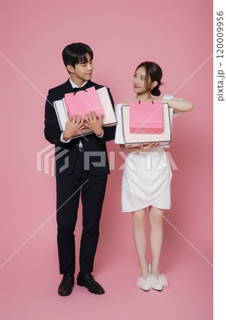 A couple wearing dresses and suits and holding shopping bags A couple wearing dresses and suits and holding shopping bags 120009956