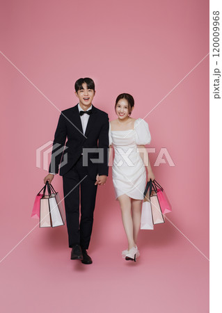 A couple wearing dresses and suits and holding shopping bags 120009968