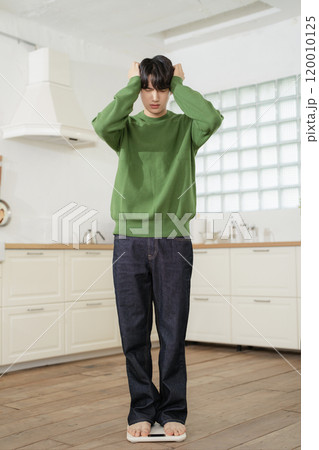 A man in his 20s measuring his weight on a scale A man in his 20s measuring his weight on a scale 120010125