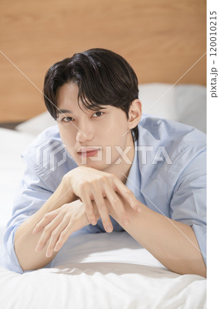 A man in his 20s posing while lying on a bed 120010215