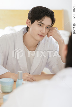 A man in his 20s sitting in front of a mirror and looking at himself for skin care 120010219
