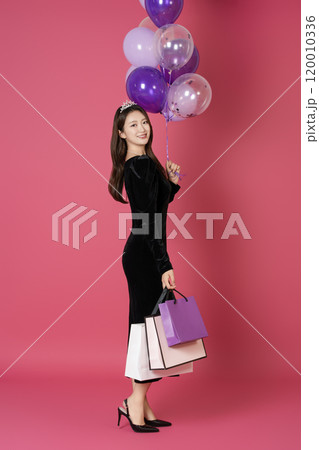 A woman in her 20s wearing a crown and posing with shopping bags and balloons A woman in her 20s wearing a crown and posing with shopping bags and balloons 120010336