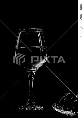 Wine glass on a black background. And a plate of fruit. On a black background. Black and white. Wine glass on a black background. And a plate of fruit. On a black background. Black and white. 120011006
