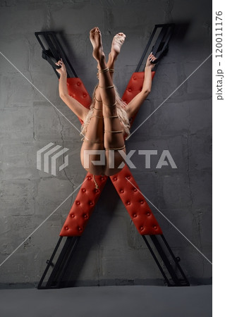 Naked woman with uplifted legs tied to cross with ropes 120011176