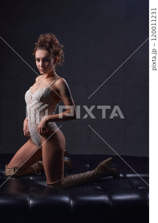 Sensual lady in provocative outfit sitting on leather couch in studio 120011231