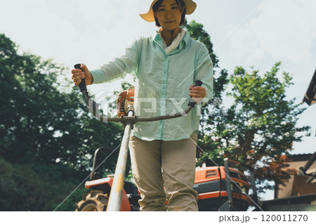 畑周りの雑草を刈払機で刈る女性 120011270