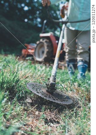畑周りの雑草を刈払機で刈る女性 120011274