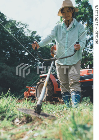 畑周りの雑草を刈払機で刈る女性 120011276