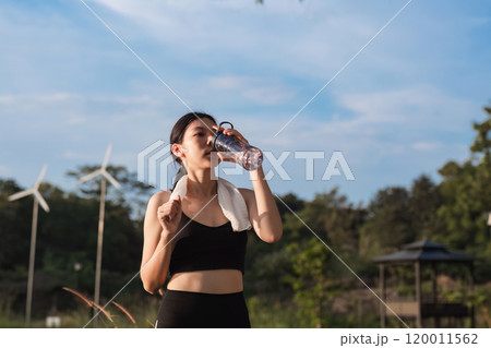 Young Woman Exercising at the Park, Drinking Water, and Enjoying a Refreshing Break on a Sunny Day Young Woman Exercising at the Park, Drinking Water, and Enjoying a Refreshing Break on a Sunny Day 120011562