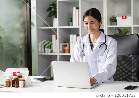 Female Doctor Providing Online Medical Advice in Modern Office Setting with Laptop and Medical Equipment 120011715