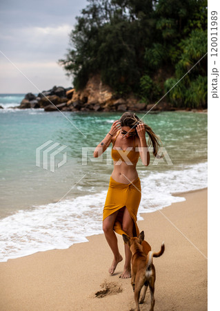 A Young Woman Happily Enjoying a Relaxing Beach Walk with Her Dog by the Ocean Waves A Young Woman Happily Enjoying a Relaxing Beach Walk with Her Dog by the Ocean Waves 120011989