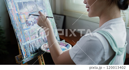 beautiful young woman artist working on painting something on a large canvas 120013402
