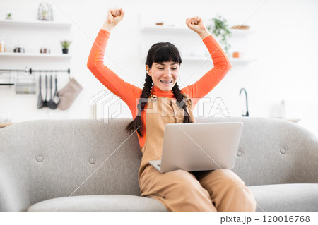 Happy woman celebrating success with laptop while working from home 120016768