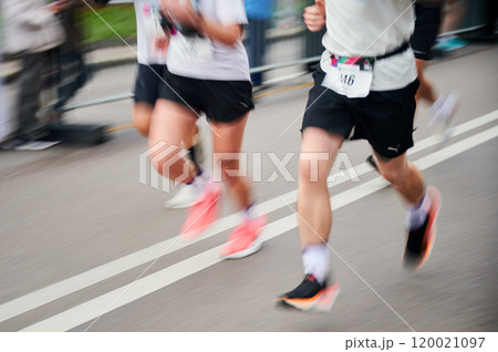 Runners in motion blur rush down the street, colorful shoes and athletic attire creating dynamic, energetic scene as they race forward with determination. 120021097