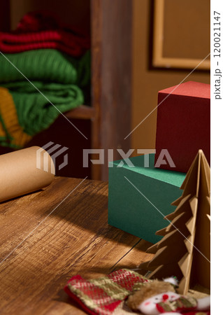 A wooden table surface holds some podiums, brown paper rolls, a paper tree, and a stocking on top, behind which is a wooden shelf containing woolen clothes. Template photo on the brown backdrop. 120021147