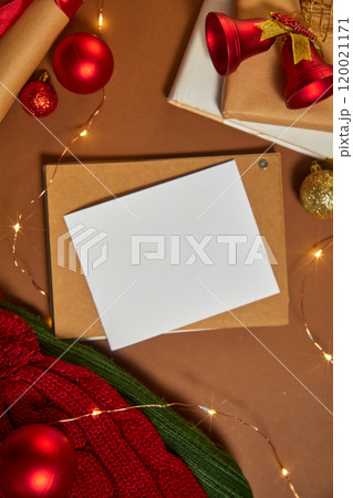 A Christmas card is laid on the paper box, surrounded by Christmas decorations. Vertical image template with minimalist Christmas concept on brown background 120021171