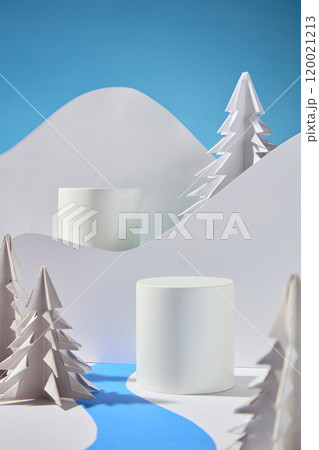 Two vacant podiums for product displays are depicted in a template image of the winter idea, with a hill of white paper on a blue background behind them and pine and green paper surrounding them. 120021213