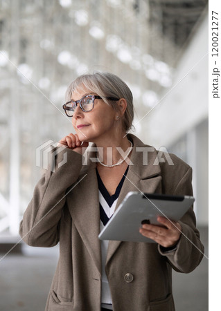 Middle-aged businesswoman thoughtfully considers her next steps while holding a tablet in a modern 120021277