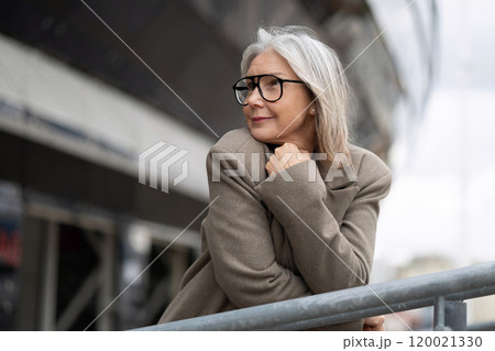 Elderly businesswoman reflects thoughtfully by the railing, showcasing a calm demeanor in an urban Elderly businesswoman reflects thoughtfully by the railing, showcasing a calm demeanor in an urban 120021330