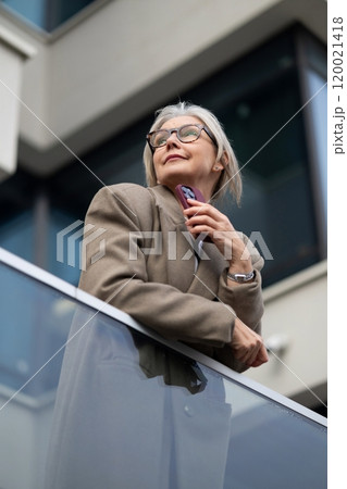 Elderly businesswoman confidently gazes at the skyline while standing on a balcony in an urban area Elderly businesswoman confidently gazes at the skyline while standing on a balcony in an urban area 120021418