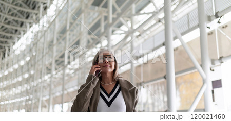 Middle-aged businesswoman in glasses talking on smartphone while walking through a modern airport 120021460