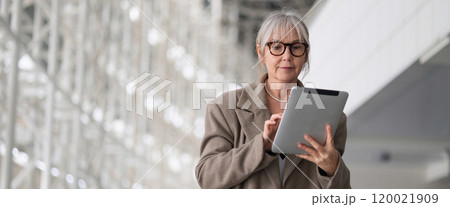 Middle-aged businesswoman using a tablet while standing in a modern office environment during Middle-aged businesswoman using a tablet while standing in a modern office environment during 120021909