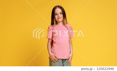 Stylish little girl, dressed casual attire, with smiling expression looking at camera, posing against yellow studio background. Stylish little girl, dressed casual attire, with smiling expression looking at camera, posing against yellow studio background. 120022946