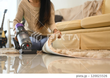Young woman doing housework, vacuuming floor with a cordless vacuum cleaner 120023326