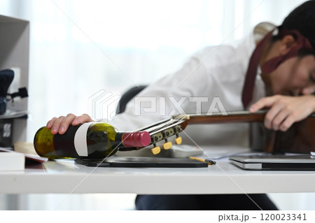 Drunk employee sleeping on desk with a bottle of wine and a guitar Drunk employee sleeping on desk with a bottle of wine and a guitar 120023341