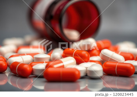 Scattered medical pills, capsules and an overturned vial 120023445