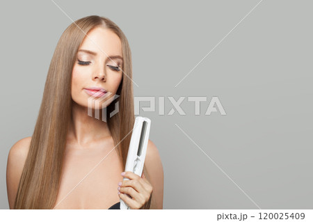 Close-up portrait of fashion model woman using hair straighteners iron on white background. Close-up portrait of fashion model woman using hair straighteners iron on white background. 120025409