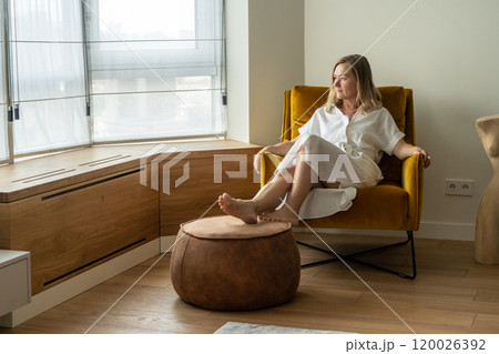 woman in a white dress sits on a chair in a hotel and looks out the window woman in a white dress sits on a chair in a hotel and looks out the window 120026392