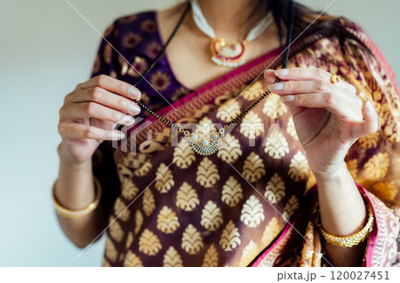 Dressed in beautiful saree, Indian woman delicately putting traditional jewellery necklace getting ready for ethnic festive celebration. Indian culture, ritual holiday in modern life. Selective focus. Dressed in beautiful saree, Indian woman delicately putting traditional jewellery necklace getting ready for ethnic festive celebration. Indian culture, ritual holiday in modern life. Selective focus. 120027451
