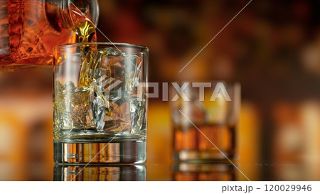 Freeze motion of pouring whisky into glass . Bar with bottles on background. 120029946