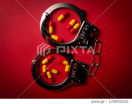 Top view metal hand cuff and medical pill on a red background. Top view metal hand cuff and medical pill on a red background. 120030581