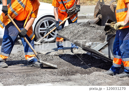 Workers repairing a road with asphalt under the midday sun in an urban setting 120031270