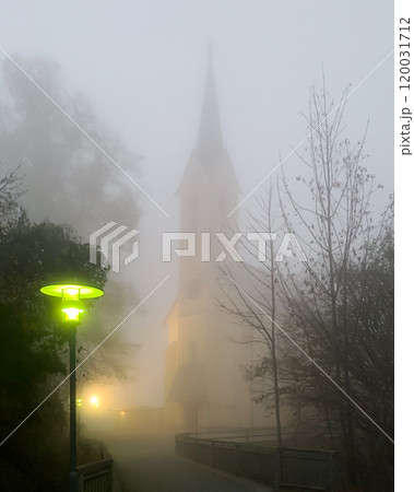 Church in thick fog with green lantern. Guggenthal branch church, in the fog of a November evening. Roman Catholic church dedicated to the Holy Cross in the Salzburg municipality of Koppl, Austria. 120031712