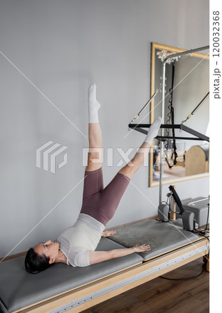 A Woman Engaged in Practicing Pilates Using Reformer Exercise Equipment for Fitness A Woman Engaged in Practicing Pilates Using Reformer Exercise Equipment for Fitness 120032368